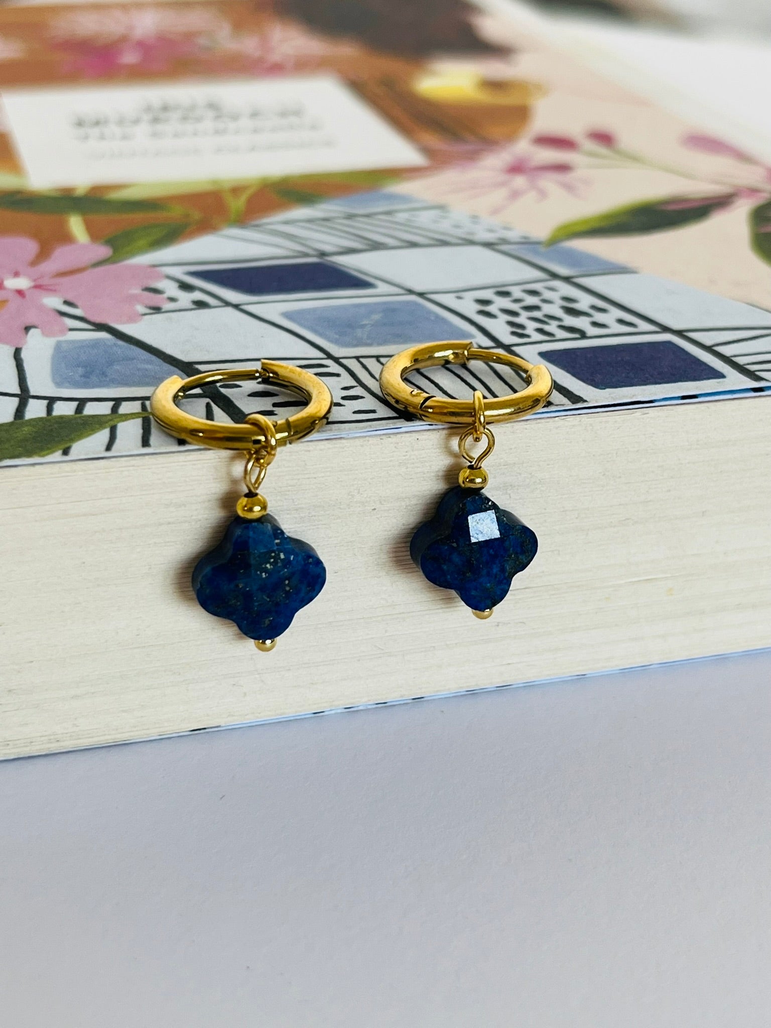 Gold hoop earrings with blue stone drops on a floral card background