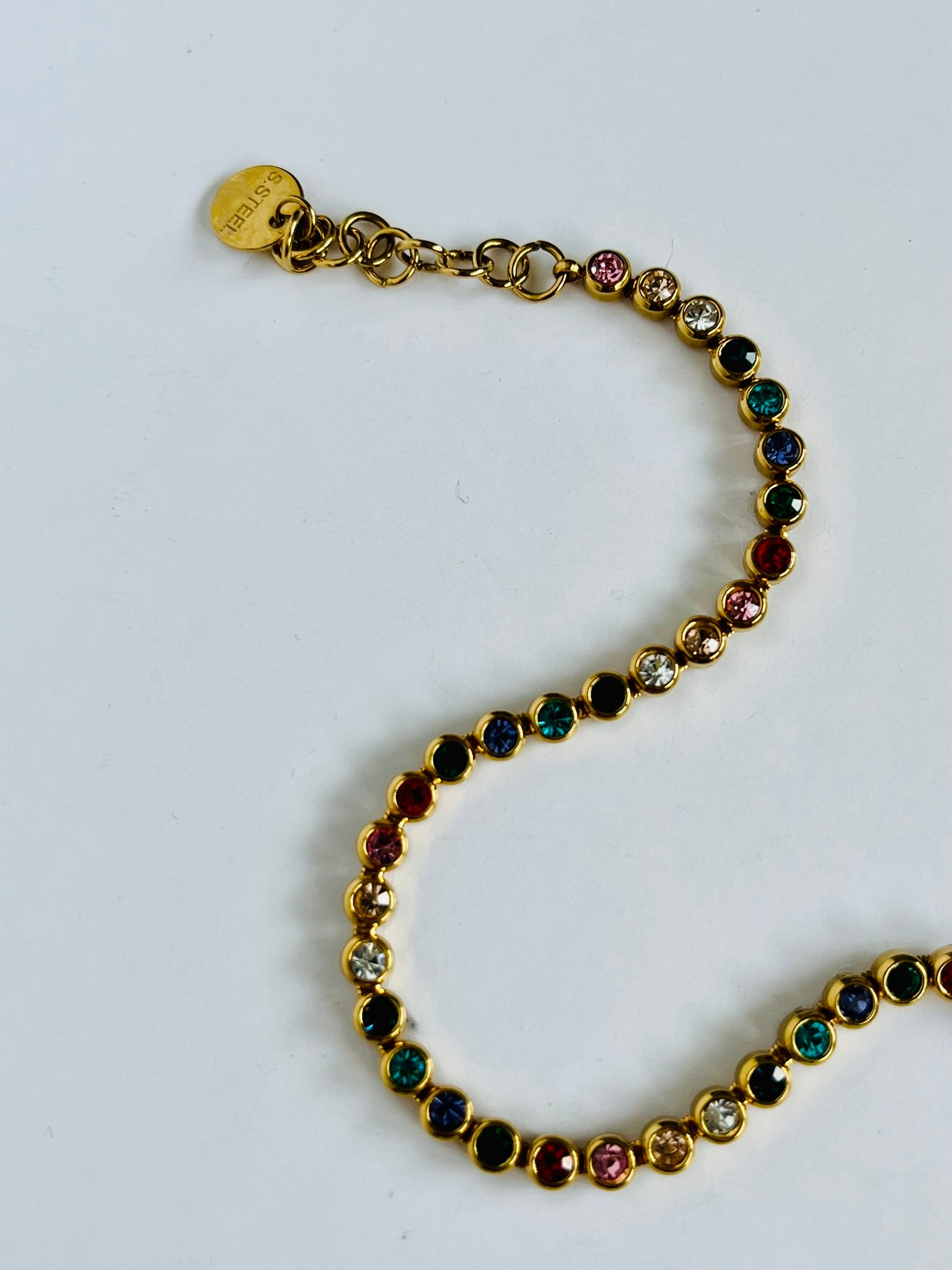 Gold bracelet with multicolored gemstones on a white background