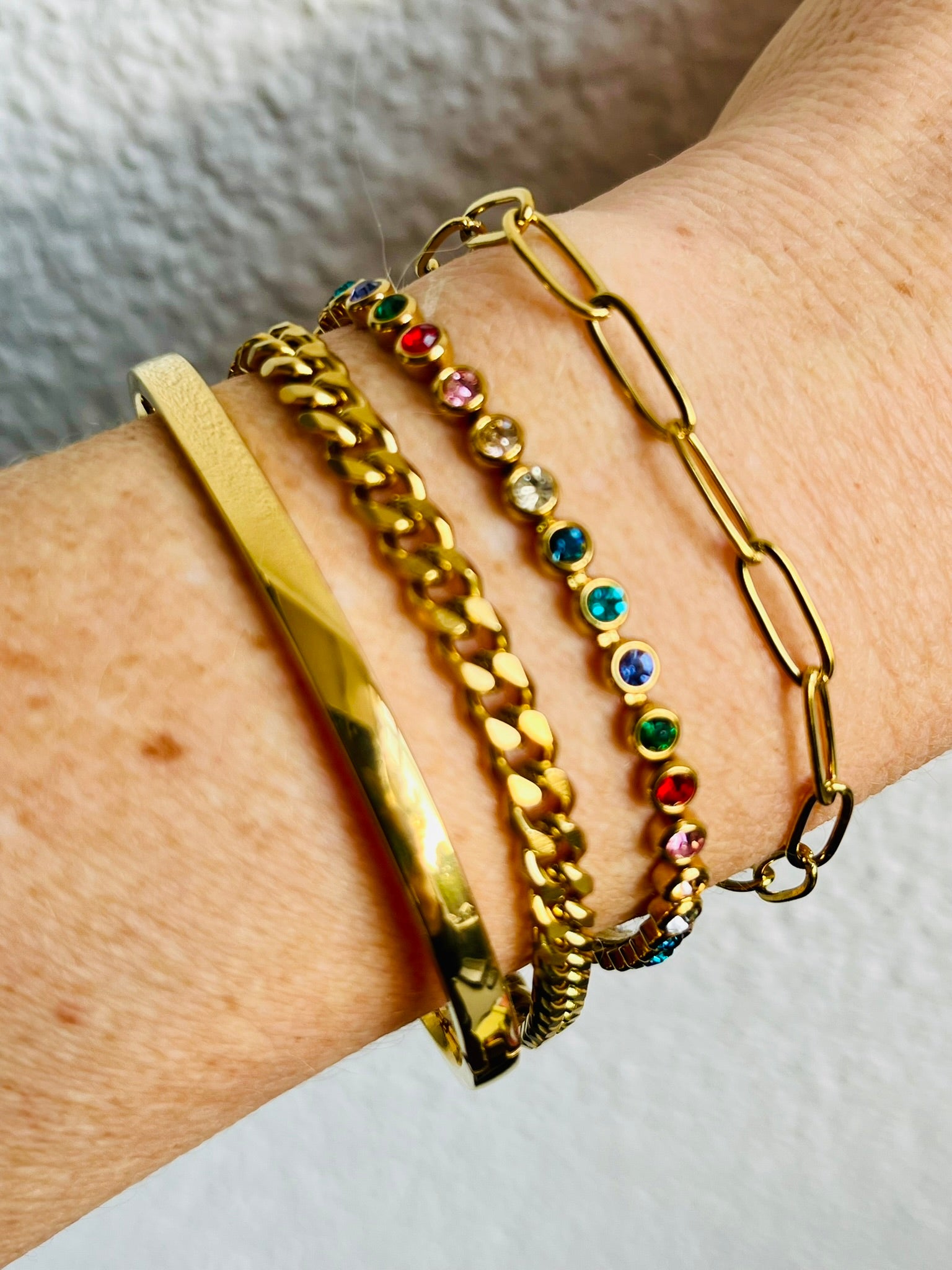 Gold bracelets with colorful beads on a wrist against a neutral background