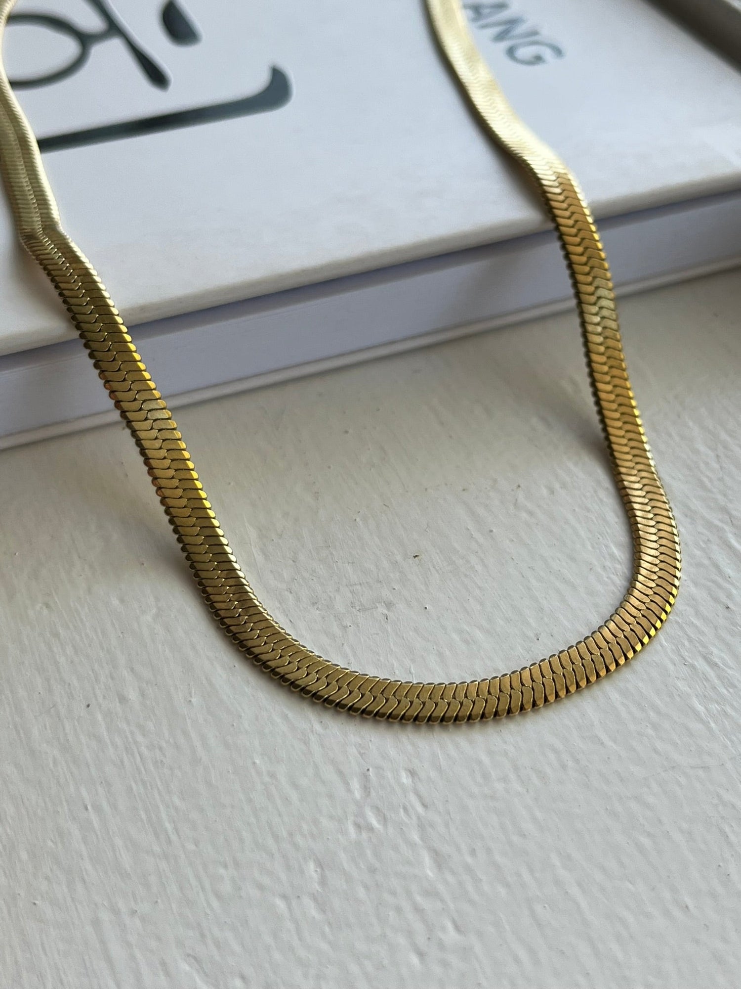 A close up of a gold paper clip necklace that is made from gold plated stainless steel. It is waterproof, tarnish proof and hypoallergenic. The etched design gives the necklace a beautiful shimmer.