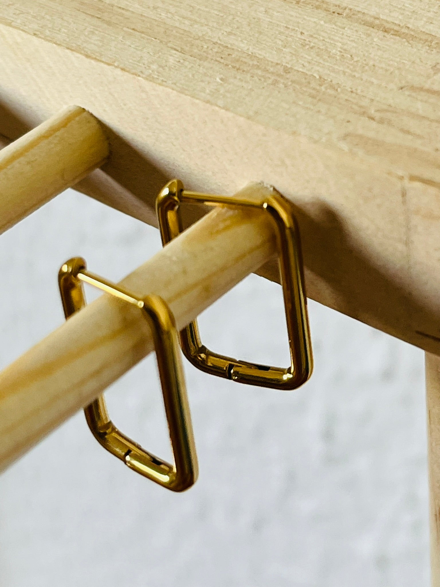 A close up of rectangular shape gold hoop earrings, that are edgy and stylish to wear.